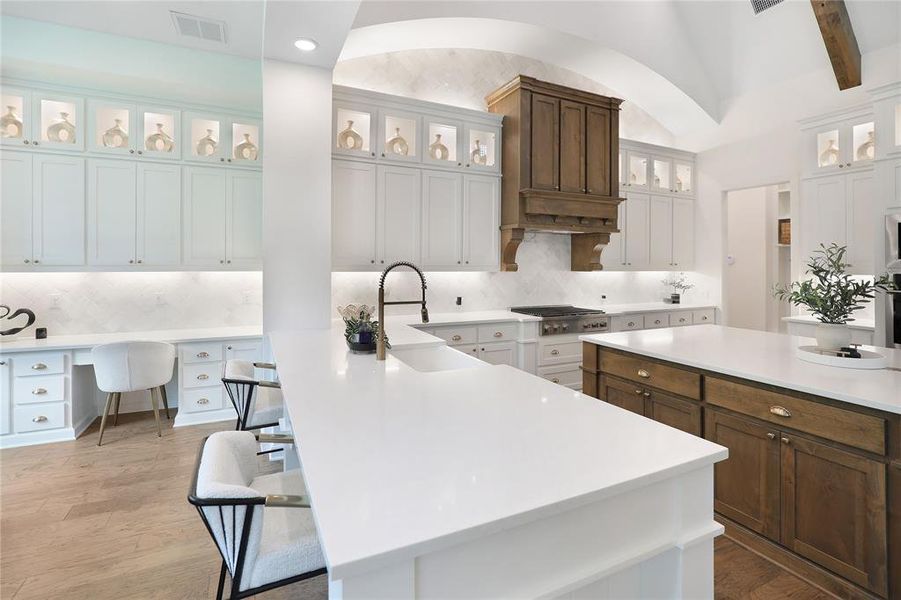 Spacious kitchen featuring two large islands with white countertops, extensive white cabinetry with upper glass-front display cabinets, and a built-in desk area