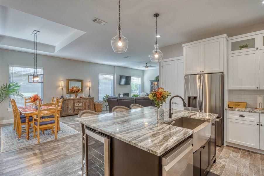 Kitchen featuring pendant lighting, light stone counters, light wood finished floors, wine cooler, and white cabinets