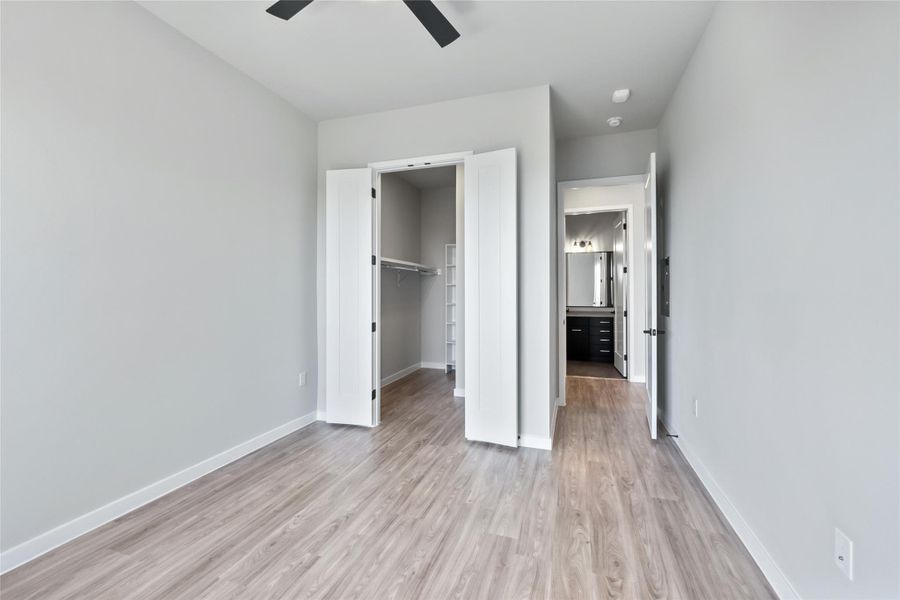 Unfurnished bedroom with light wood-style floors, a closet, a walk in closet, and a ceiling fan