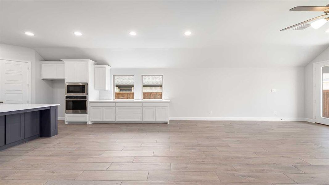 Unfurnished living room featuring plenty of natural light, ceiling fan, lofted ceiling, and light hardwood / wood-style floors