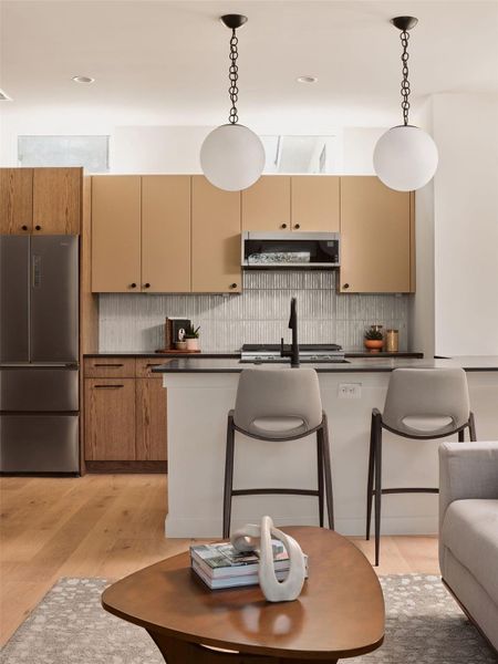 Kitchen featuring dark countertops, a kitchen breakfast bar, stainless steel appliances, pendant lighting, and light wood finished floors