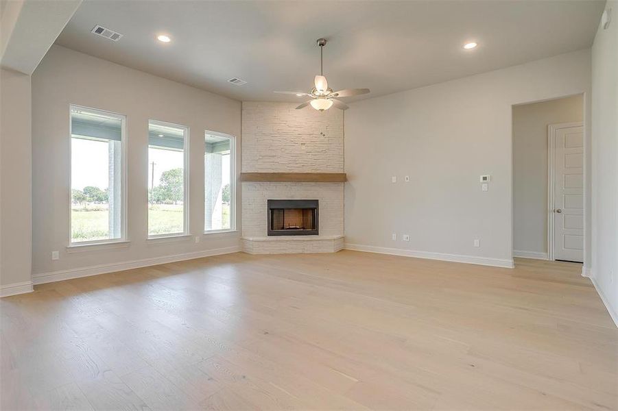 Unfurnished living room with ceiling fan, a fireplace, and light hardwood / wood-style flooring