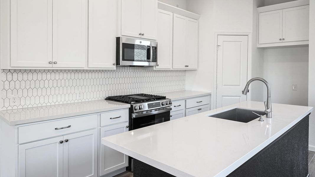 Kitchen with a center island with sink, white cabinets, decorative backsplash, stainless steel appliances, and light stone counters Kitchen with a center island with sink, white cabinets, decorative backsplash, stainless steel appliances, and light stone counters