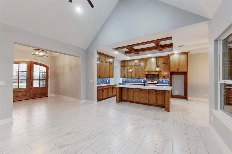 Kitchen with french doors, custom range hood, pendant lighting, decorative backsplash, and an island with sink