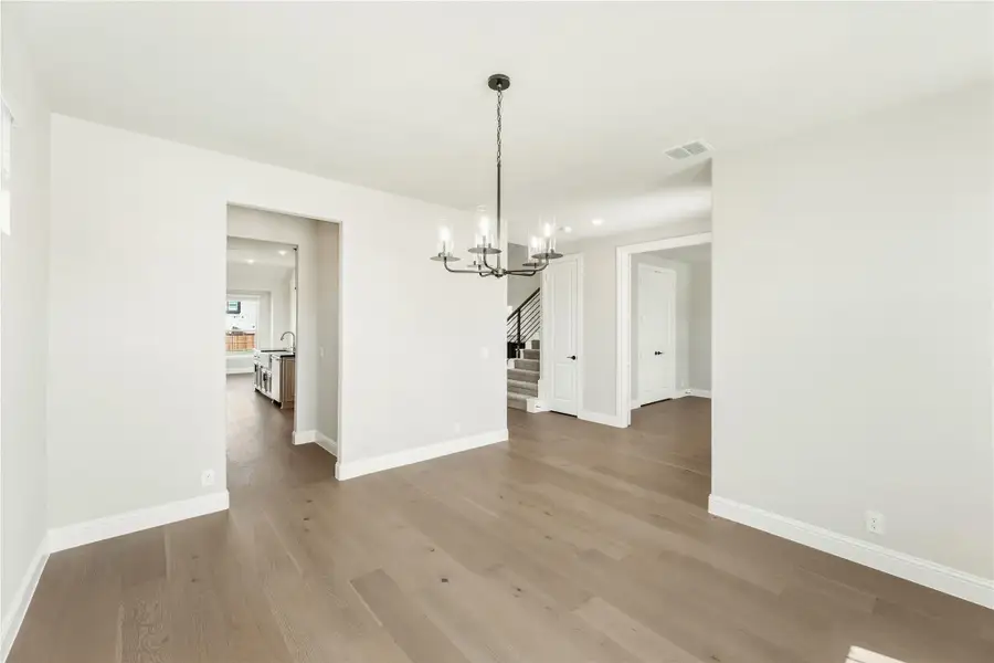 Empty dining room with hardwood floors, chandelier, and open view to kitchen and staircase Empty dining room with hardwood floors, chandelier, and open view to kitchen and staircase