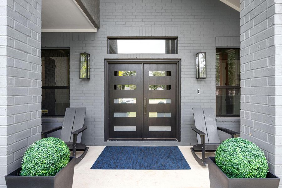 Modern front entrance with a sleek dark double door featuring horizontal glass panels. Flanked by tall windows and contemporary sconces, for a welcoming touch. Modern front entrance with a sleek dark double door featuring horizontal glass panels. Flanked by tall windows and contemporary sconces, for a welcoming touch.
