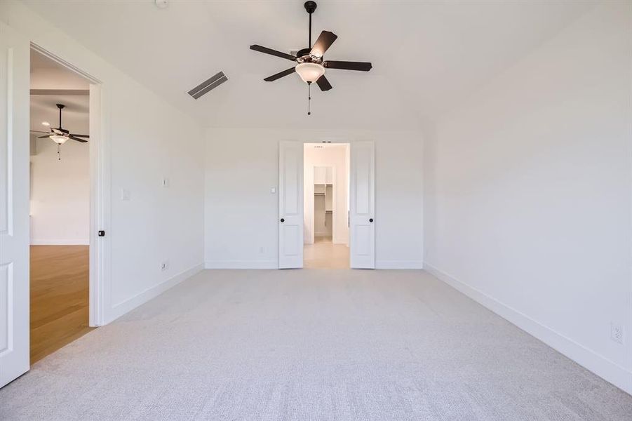 Unfurnished bedroom with a walk in closet, light carpet, lofted ceiling, baseboards, and ceiling fan Unfurnished bedroom with a walk in closet, light carpet, lofted ceiling, baseboards, and ceiling fan