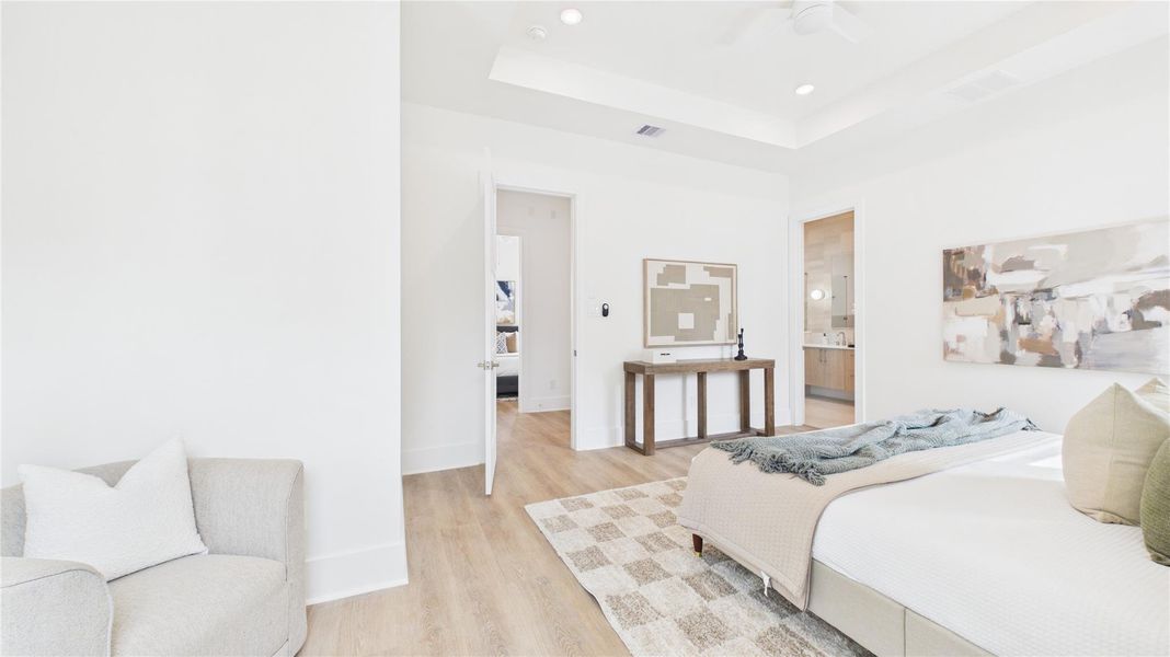 Bright and spacious bedroom with modern decor, featuring light wood flooring, a cozy armchair, and a stylish bed. The room is complemented by abstract art and a clean, open layout leading to an en-suite bathroom.