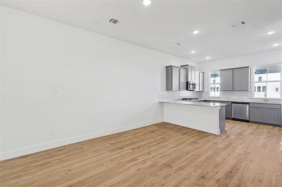 Kitchen featuring gray cabinetry, tasteful backsplash, a peninsula, light wood-style flooring, and appliances with stainless steel finishes