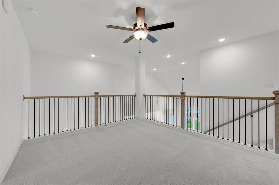 Open loft space featuring light gray carpeting, white walls, recessed lighting, and a ceiling fan