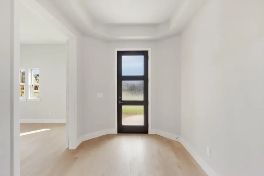Entryway with black glass-panel door, tray ceiling, and light hardwood floors