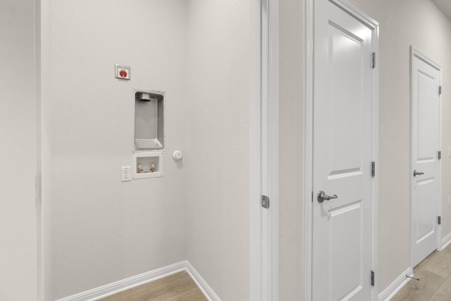 Dedicated utility space featuring light-colored walls, light wood-style flooring, and white baseboards
