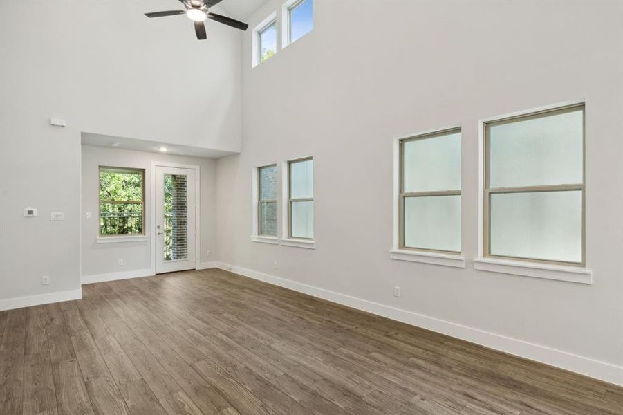 living room with a towering ceiling, wood finished floors, a ceiling fan, and baseboards