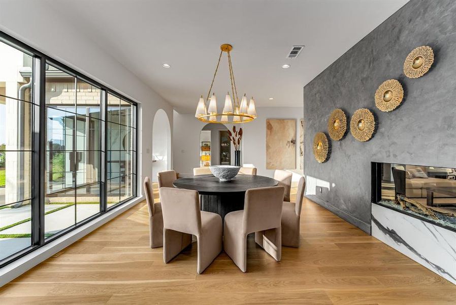 Dining area featuring light wood-style floors, arched walkways, recessed lighting, a premium fireplace, and an accent wall Dining area featuring light wood-style floors, arched walkways, recessed lighting, a premium fireplace, and an accent wall