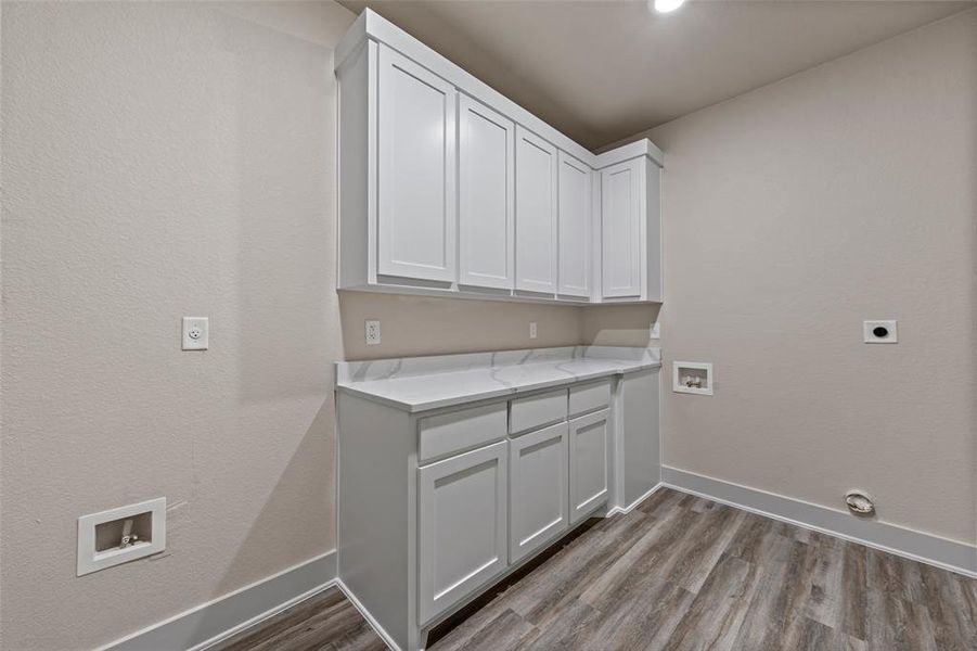 Laundry room featuring a white shaker-style cabinetry, a solid surface countertop, wood-finish flooring, recessed lighting, and neutral wall paint Laundry room featuring a white shaker-style cabinetry, a solid surface countertop, wood-finish flooring, recessed lighting, and neutral wall paint