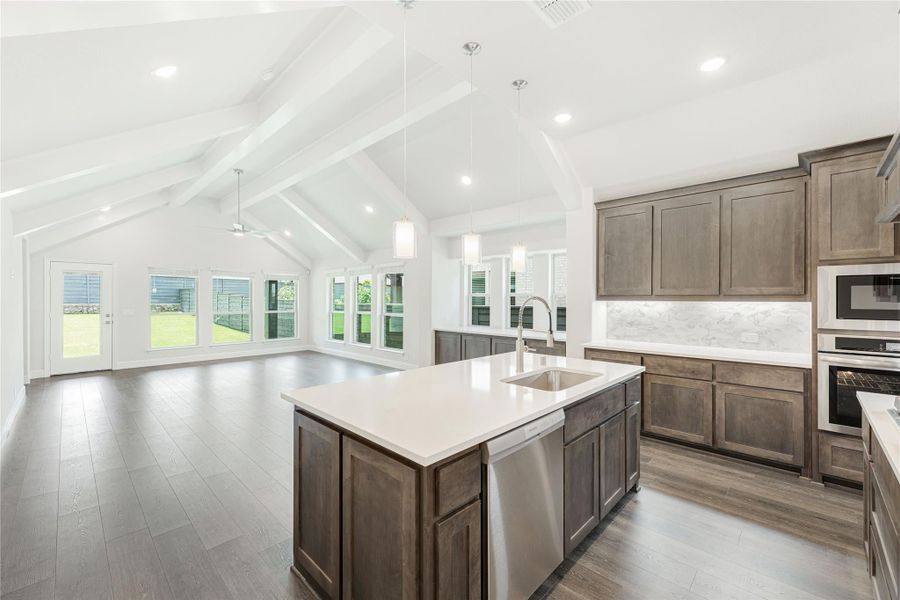Open kitchen with dark wood cabinets, large island, and vaulted beamed ceiling open to living area with hardwood floors Open kitchen with dark wood cabinets, large island, and vaulted beamed ceiling open to living area with hardwood floors