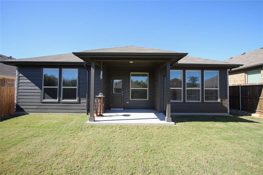 Rear view of property featuring a lush yard and covered patio.