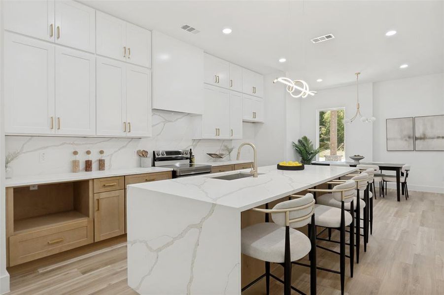 Open-concept kitchen featuring an expansive island with seating, a waterfall countertop, integrated sink, and white upper cabinetry Open-concept kitchen featuring an expansive island with seating, a waterfall countertop, integrated sink, and white upper cabinetry