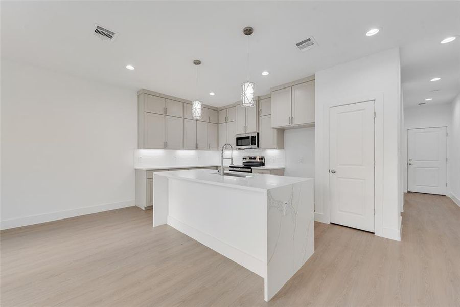 Kitchen with an island with sink, light stone counters, decorative light fixtures, light wood-style floors, and recessed lighting Kitchen with an island with sink, light stone counters, decorative light fixtures, light wood-style floors, and recessed lighting