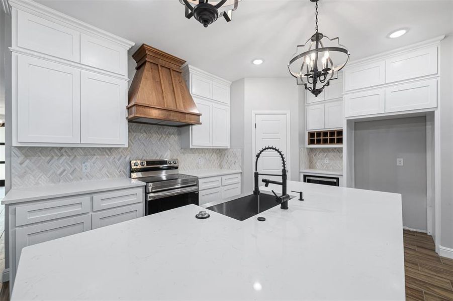 Kitchen featuring pendant lighting, stainless steel electric range, premium range hood, sink, and white cabinetry