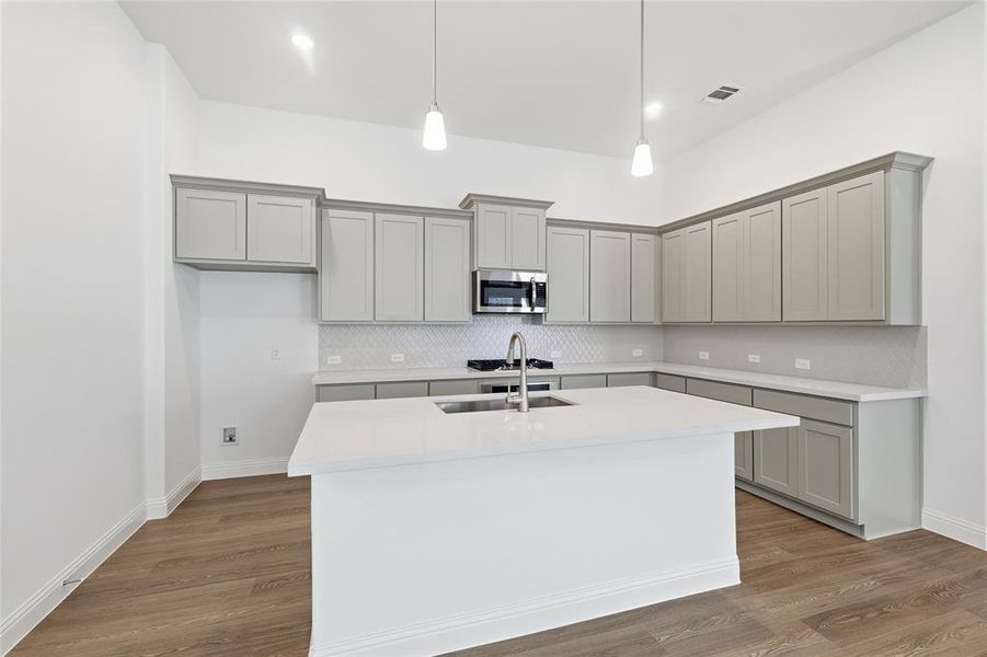 Kitchen featuring gray cabinets, decorative light fixtures, stainless steel microwave, and decorative backsplash