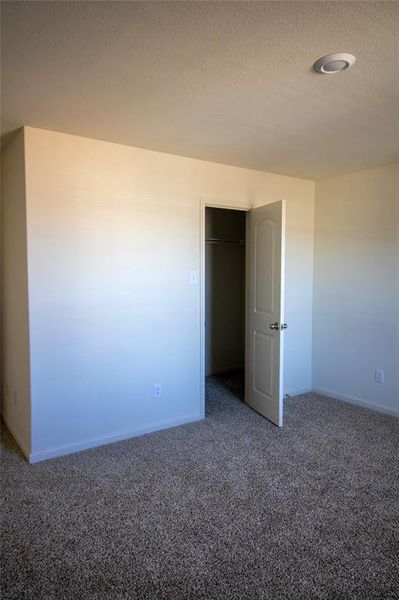 Unfurnished bedroom with dark carpet, a closet, and a textured ceiling