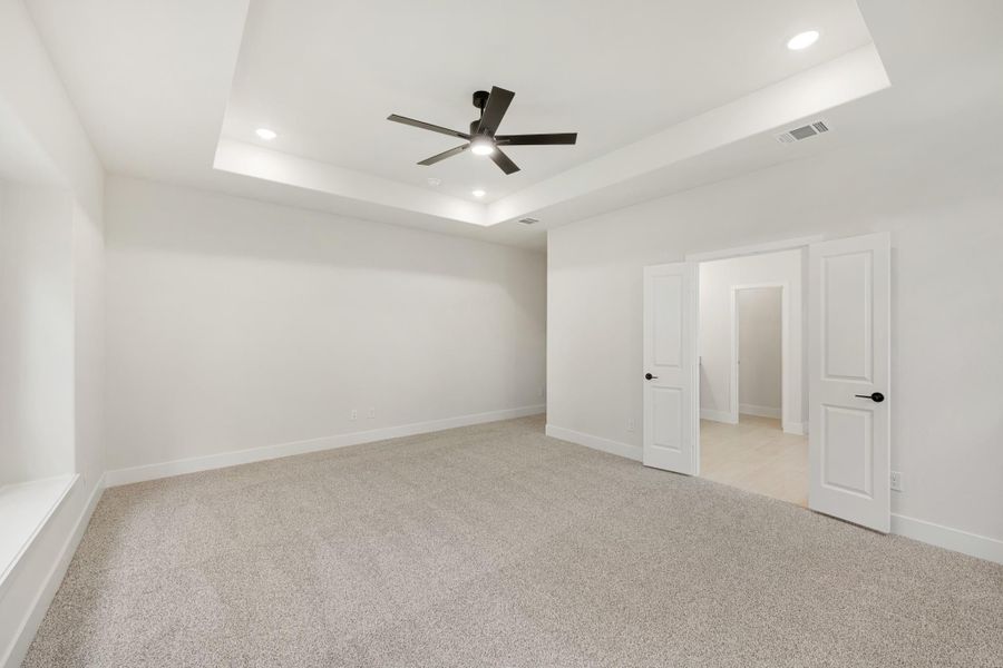 Empty bedroom with tray ceiling, ceiling fan, carpet flooring, and two white doors