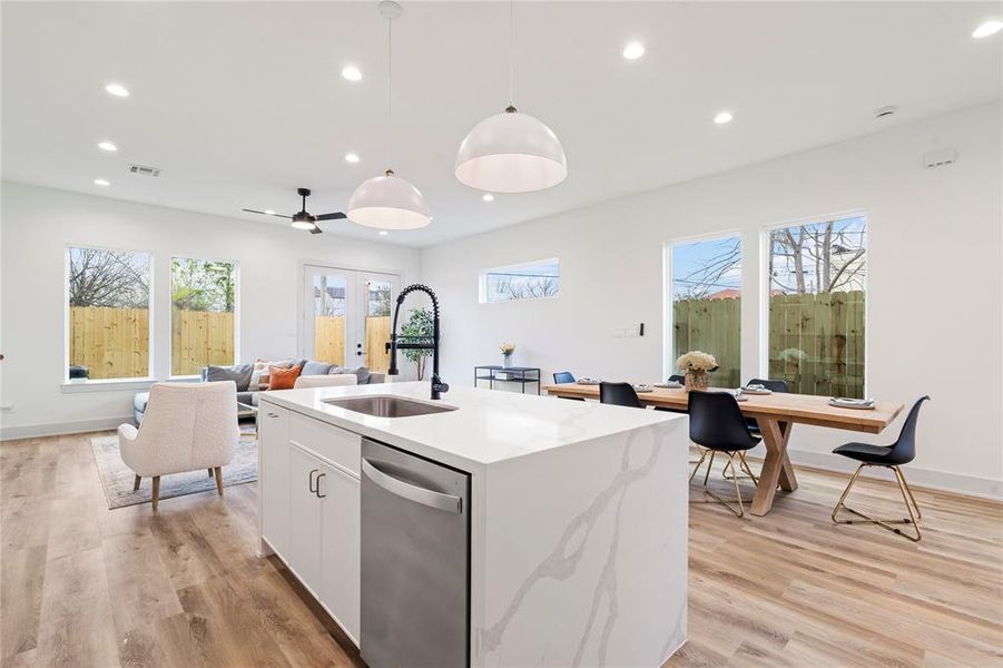 The kitchen is illuminated by dome pendant lighting over the island and recessed LED ceiling lights, enhancing the bright and airy feel.