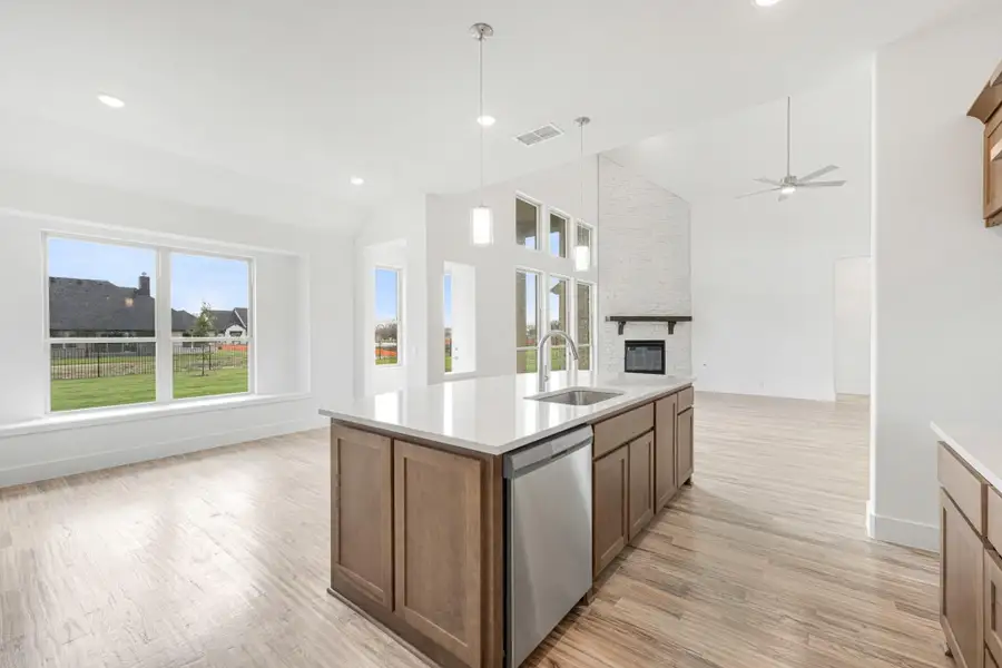 Open kitchen with wood island, quartz countertop, and stainless dishwasher, open to living area with brick fireplace and vaulted ceiling. Open kitchen with wood island, quartz countertop, and stainless dishwasher, open to living area with brick fireplace and vaulted ceiling.
