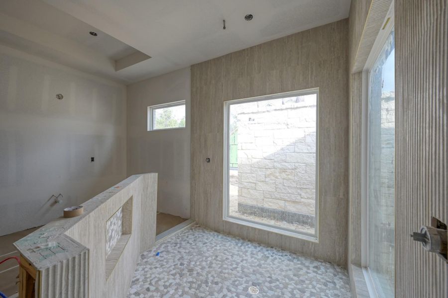 The primary bathroom is a private spa-like escape, featuring a serene soaking tub and a spacious walk-through shower with dual entries, a rain head, and views of a secluded garden—creating a true resort-style experience.