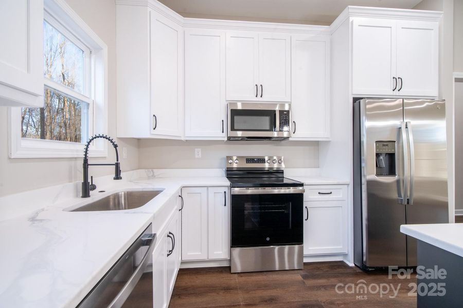 Bright kitchen showcasing quartz countertops, white cabinetry, and a full stainless steel appliance package.