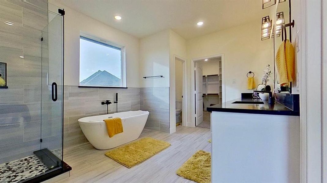 Bathroom featuring a walk in closet, a soaking tub, a shower stall, vanity, and tile walls Bathroom featuring a walk in closet, a soaking tub, a shower stall, vanity, and tile walls