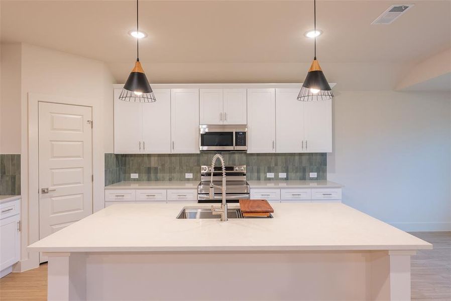 Kitchen featuring light wood finished floors, decorative backsplash, white cabinets, stainless steel appliances, and light stone countertops