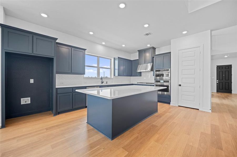 Kitchen featuring light hardwood / wood-style flooring, decorative backsplash, sink, stainless steel double oven, and a center island