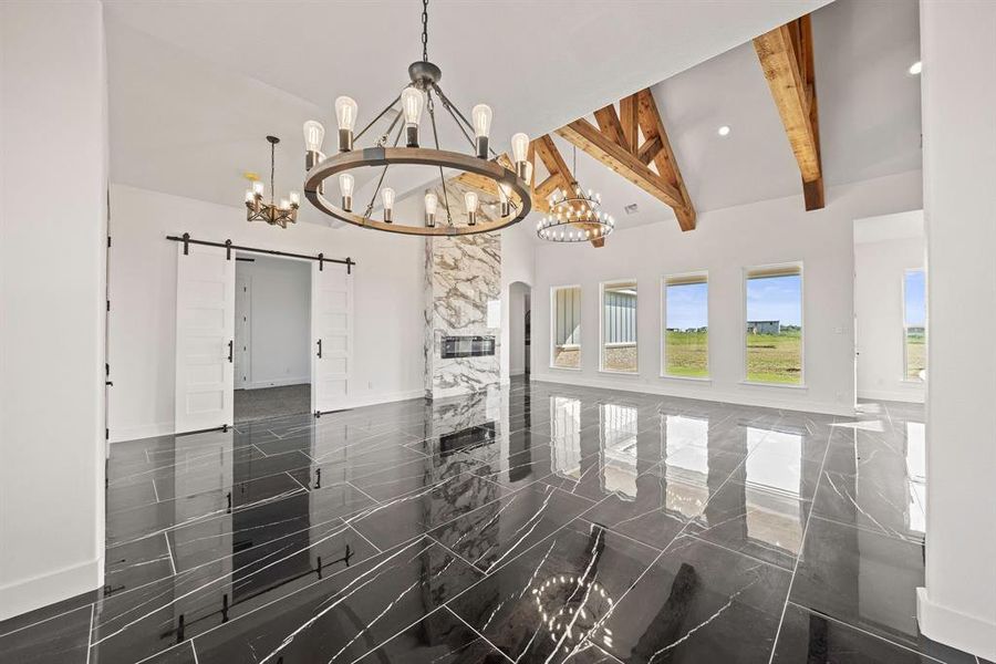 Empty room with a chandelier, a barn door, beam ceiling, high vaulted ceiling, and baseboards Empty room with a chandelier, a barn door, beam ceiling, high vaulted ceiling, and baseboards
