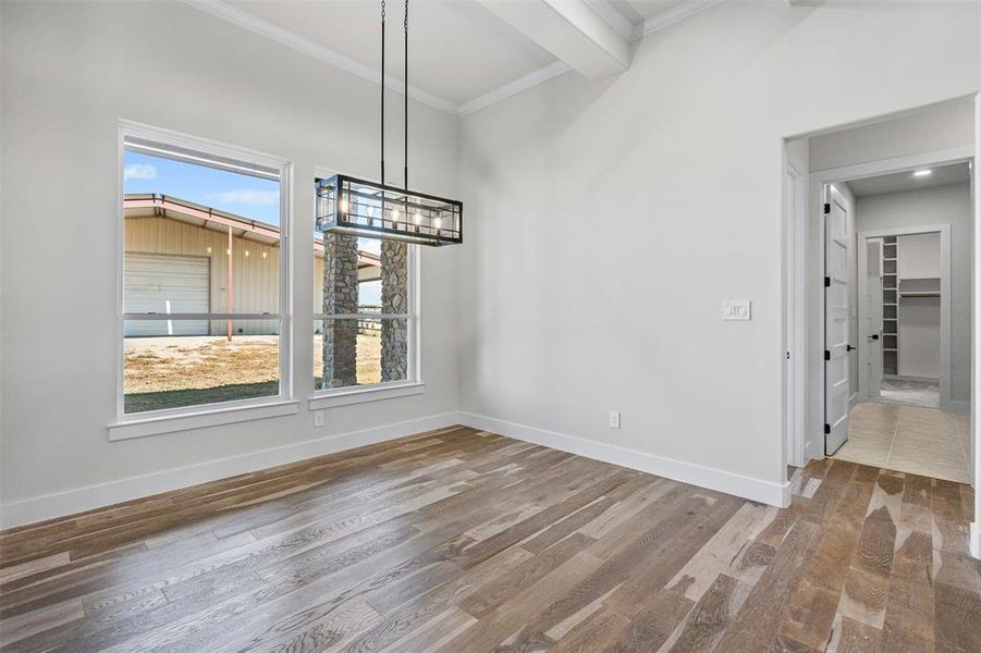 Unfurnished dining area featuring wood finished floors, crown molding, and beamed ceiling