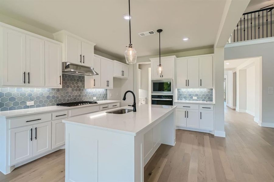 Kitchen featuring decorative backsplash, a kitchen island with sink, hanging light fixtures, sink, and white cabinets