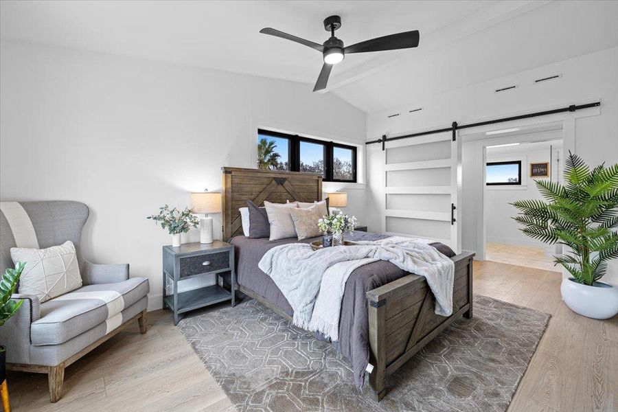 Bedroom featuring multiple windows, lofted ceiling with beams, a barn door, and wood finished floors