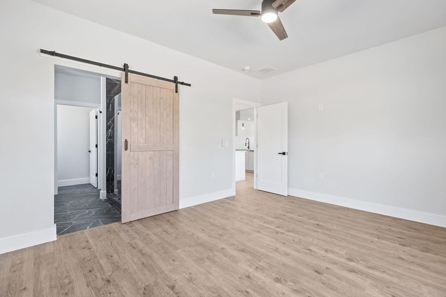 Unfurnished bedroom with a barn door, a ceiling fan, and wood finished floors