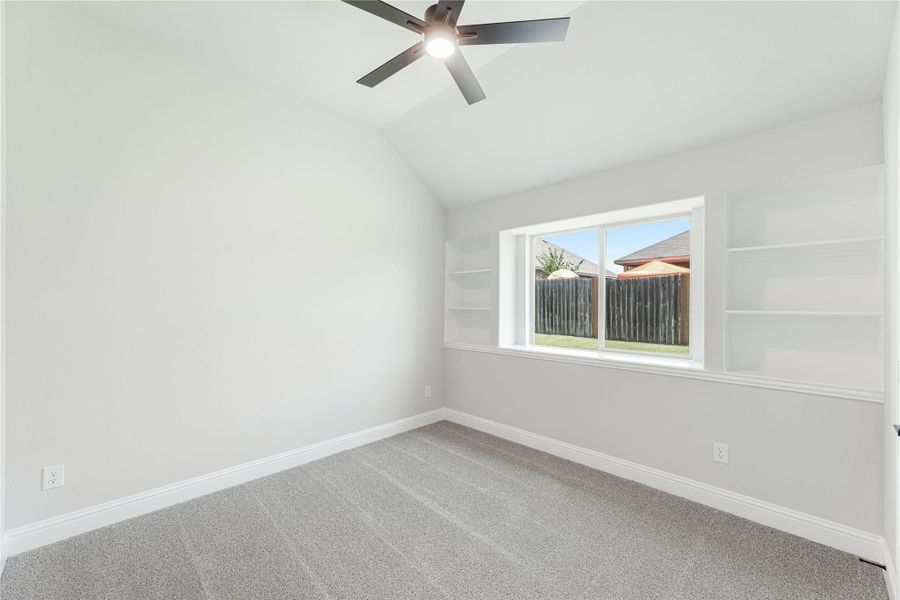 Empty bedroom with vaulted ceiling, ceiling fan, built-in shelves, and carpet flooring Empty bedroom with vaulted ceiling, ceiling fan, built-in shelves, and carpet flooring