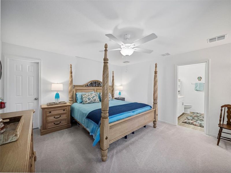 Bedroom featuring a ceiling fan, light colored carpet, visible vents, and connected bathroom