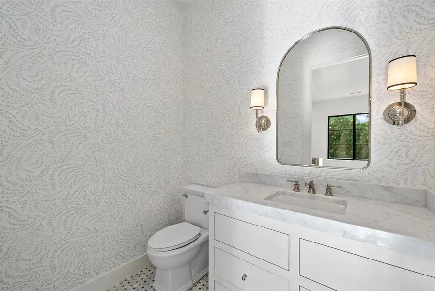 The bathroom features a white vanity with a marble countertop, an arched mirror, and white patterned wallpaper