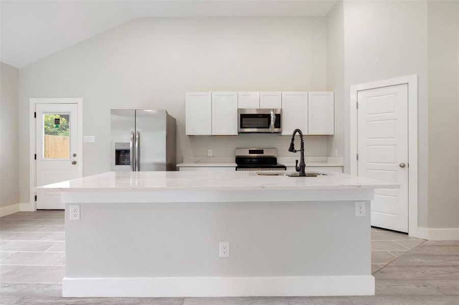 Kitchen featuring high vaulted ceiling, stainless steel appliances, a center island with sink, and sink