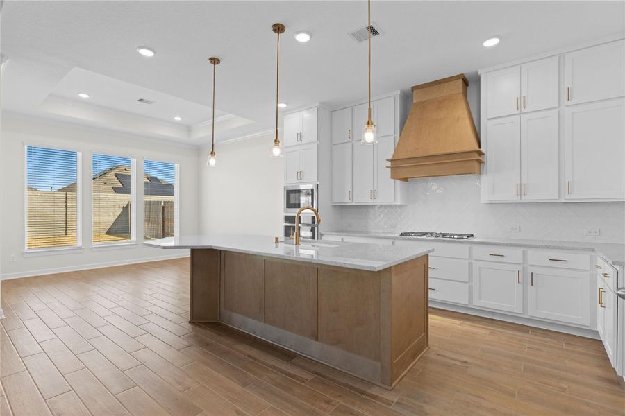The gourmet kitchen makes a stunning statement with its oversized large island, elegant pendant lighting, and seamless connection to the living and dining areas, creating a perfect setting for entertaining and everyday living, all grounded by beautiful wood like tile flooring.