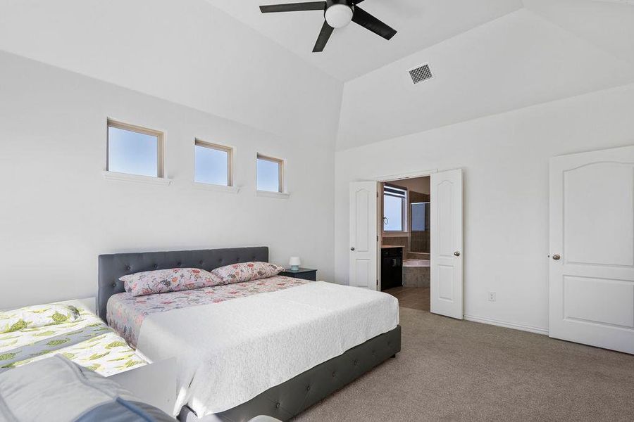 Carpeted bedroom featuring ensuite bathroom, a ceiling fan, and vaulted ceiling Carpeted bedroom featuring ensuite bathroom, a ceiling fan, and vaulted ceiling