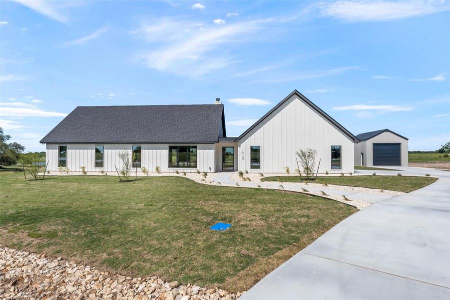 Modern inspired farmhouse featuring a front lawn, concrete driveway, a garage, board and batten siding, and a shingled roof Modern inspired farmhouse featuring a front lawn, concrete driveway, a garage, board and batten siding, and a shingled roof
