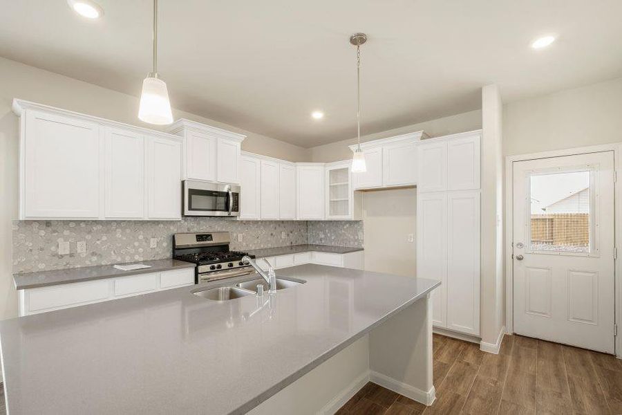 This modern kitchen is a chef's dream with its sleek Silestone Quartz countertops, custom tile backsplash, and stainless steel appliances. The large island provides ample workspace, while pendant lighting adds a touch of elegance. Spacious cabinetry ensures all your storage needs are met, creating the perfect blend of style and functionality.