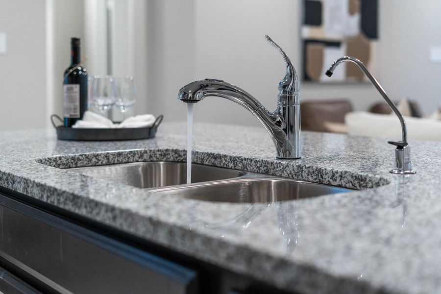 This kitchen boasts a contemporary double sink seamlessly integrated into the beautiful speckled granite countertops, offering both a primary faucet and a convenient secondary faucet for purified drinking water!