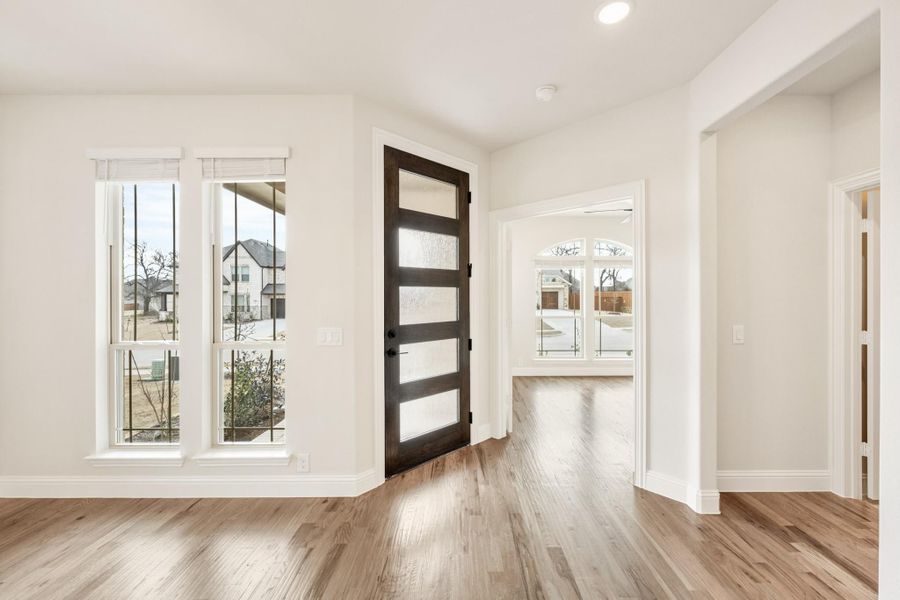 Bright entryway with dark wood glass-panel front door, hardwood floors, and white walls
