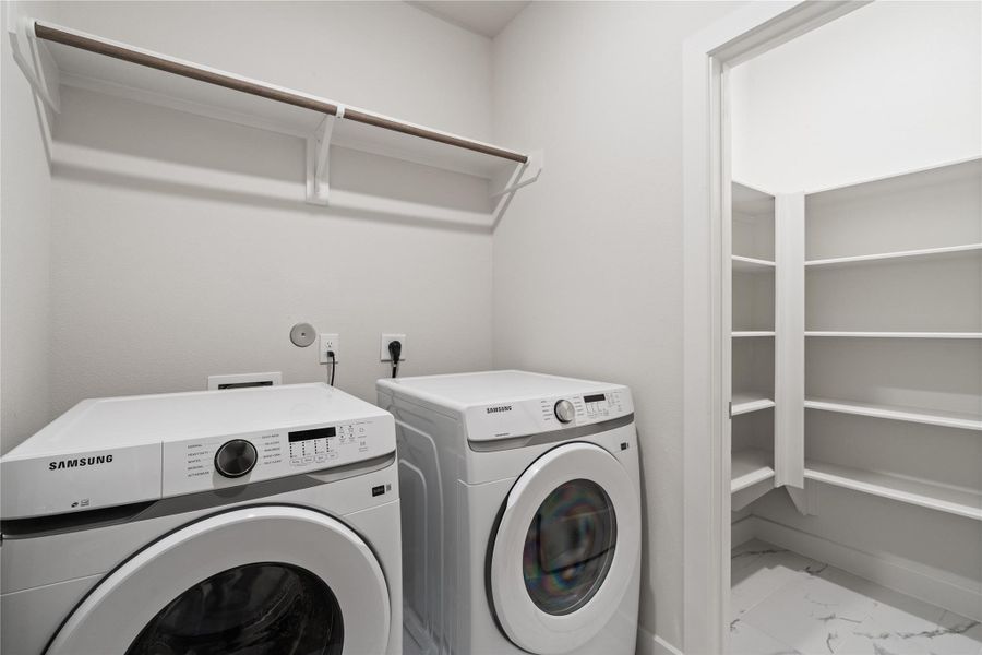 Spacious laundry room with side by side setup, upper hanging space, and a dedicated storage closet with built in shelving for added organization.
